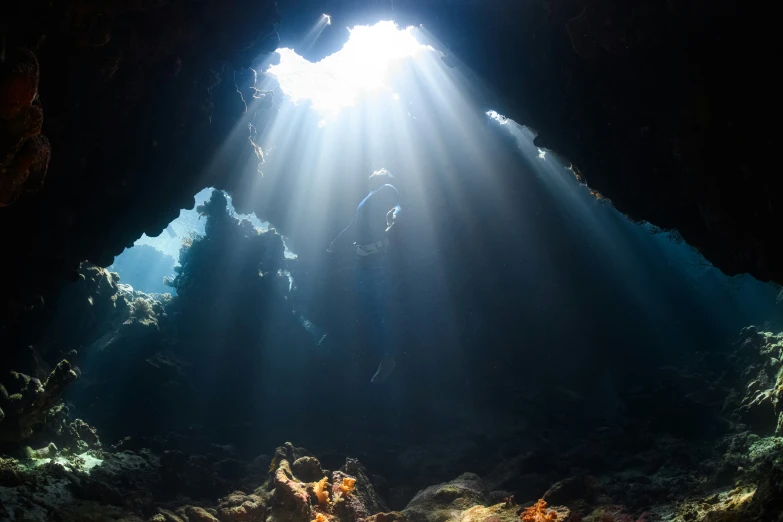 sunbeams shining into a cave underwater with coral reef