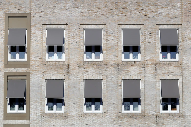 a brick wall that has seven windows, and two on each side with grey shades and blind folded open