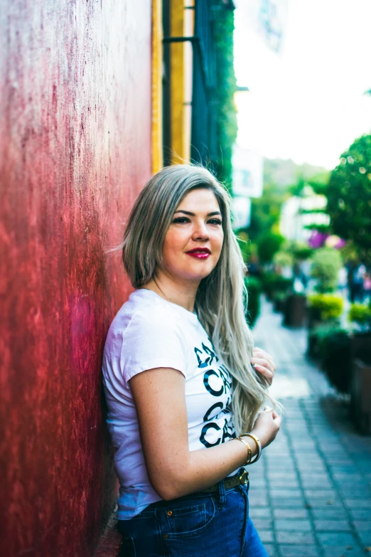 a beautiful woman leaning against the side of a red building