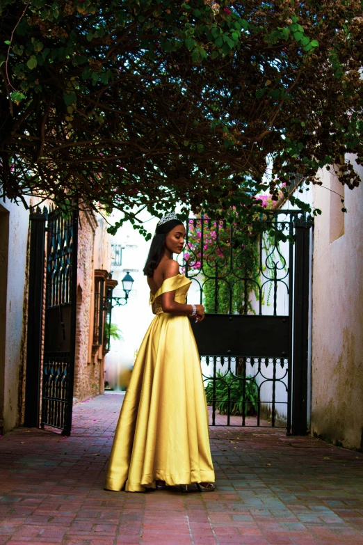 woman in long yellow dress posing near wrought iron gate