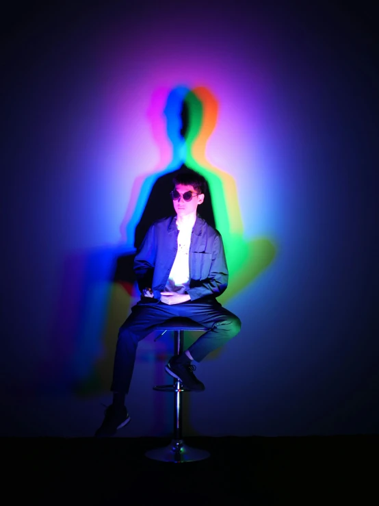 the man is seated in a chair in front of a colored shadow