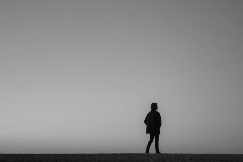 a lone man standing in a field, holding on to the umbrella