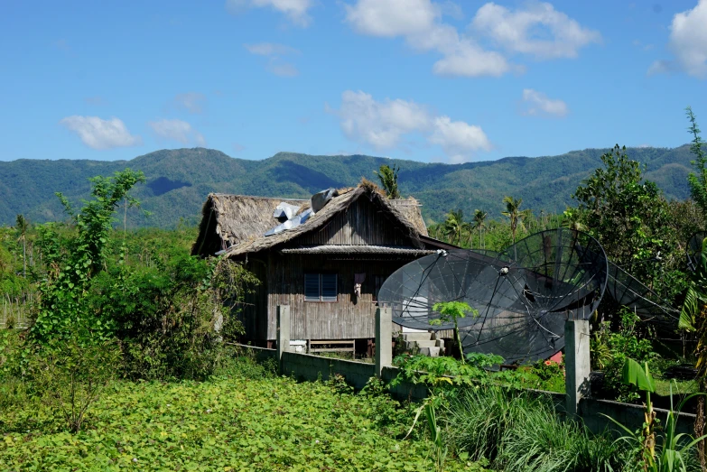 a wooden cabin with green grass and mountains behind it