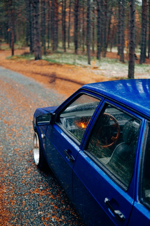 a blue car on the side of a forest road