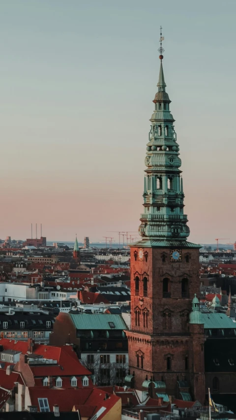 a tall steeple stands above the city below a pink sky