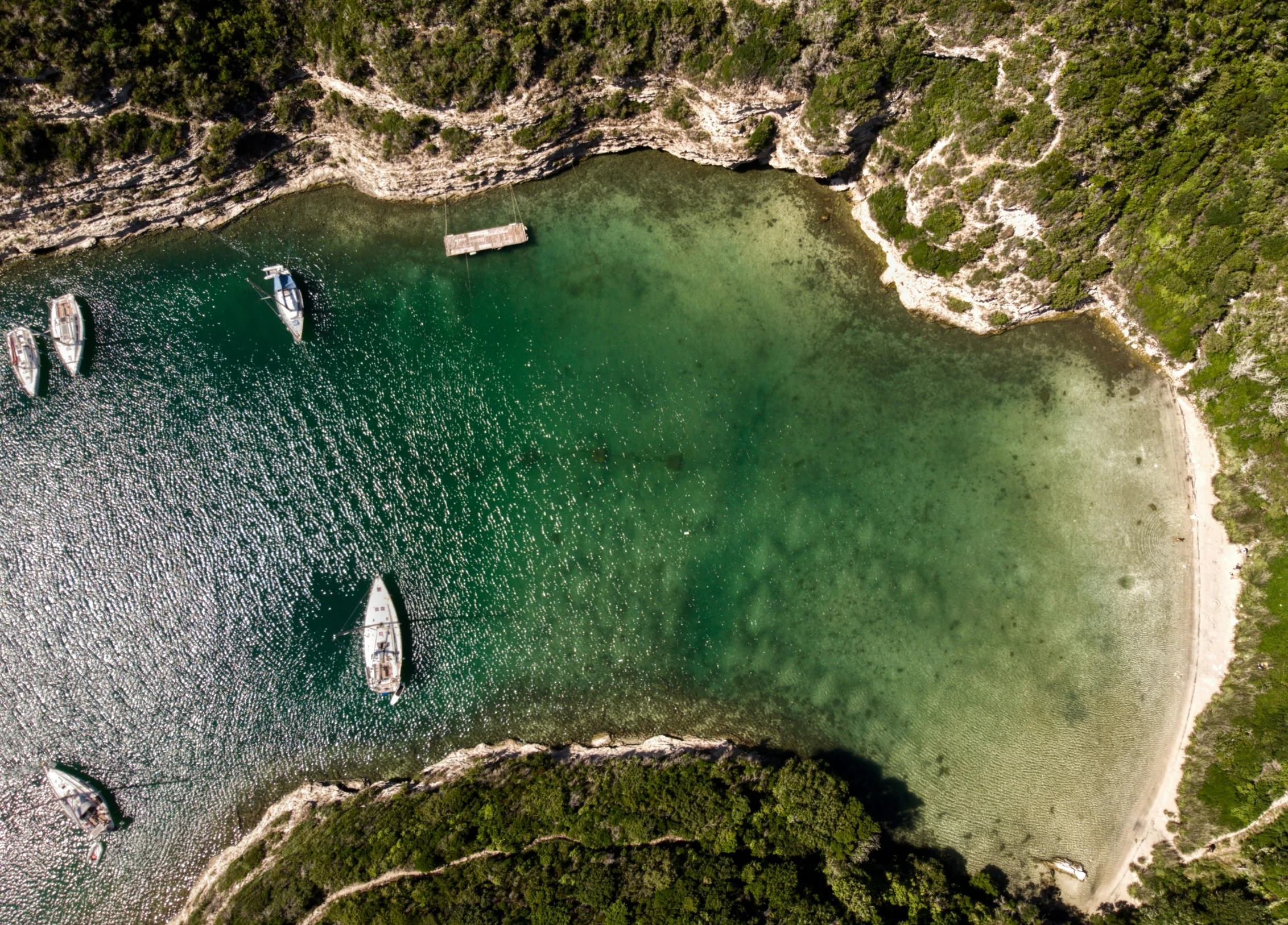 an aerial view of several sailboats anchored at a calm bay in a tropical island