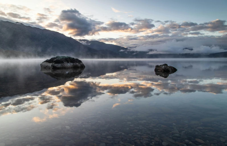 some big rocks in the water with clouds above