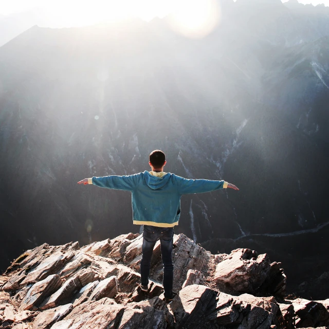 a person stands on top of rocks while arms out and a view is in the distance