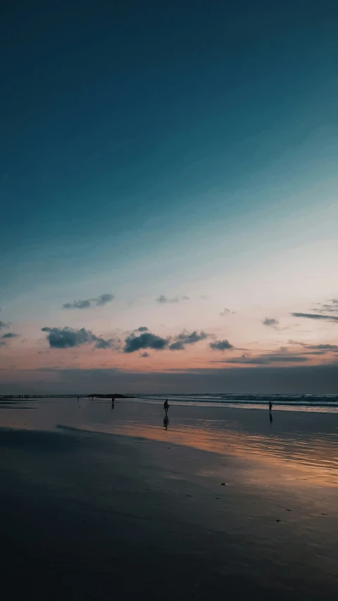 a couple of people walking on a beach at sunset