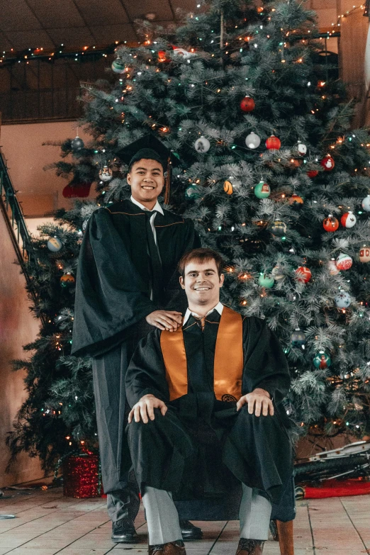 an image of two graduates in front of a christmas tree