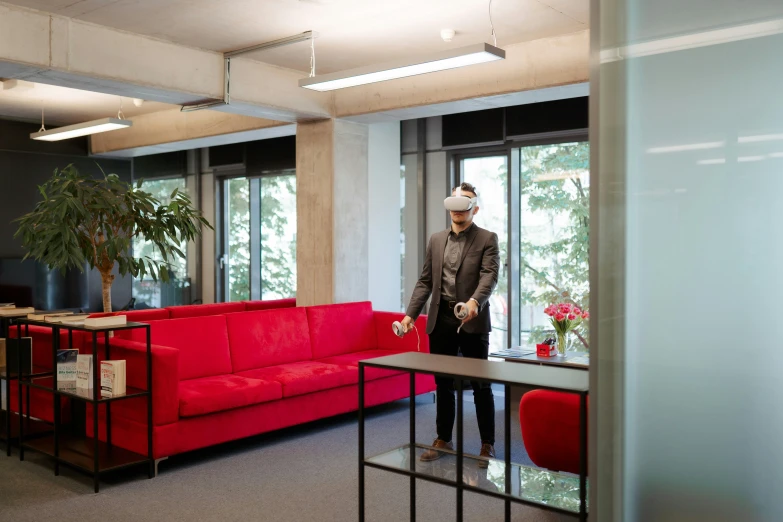 the man wearing a protective face mask walks in front of a living room with a red couch