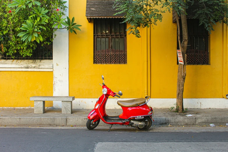 a red scooter parked near a tree next to a yellow building