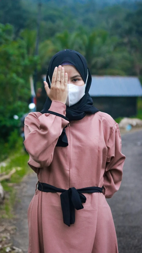 a young woman wearing a face mask and standing in front of a mountain with trees