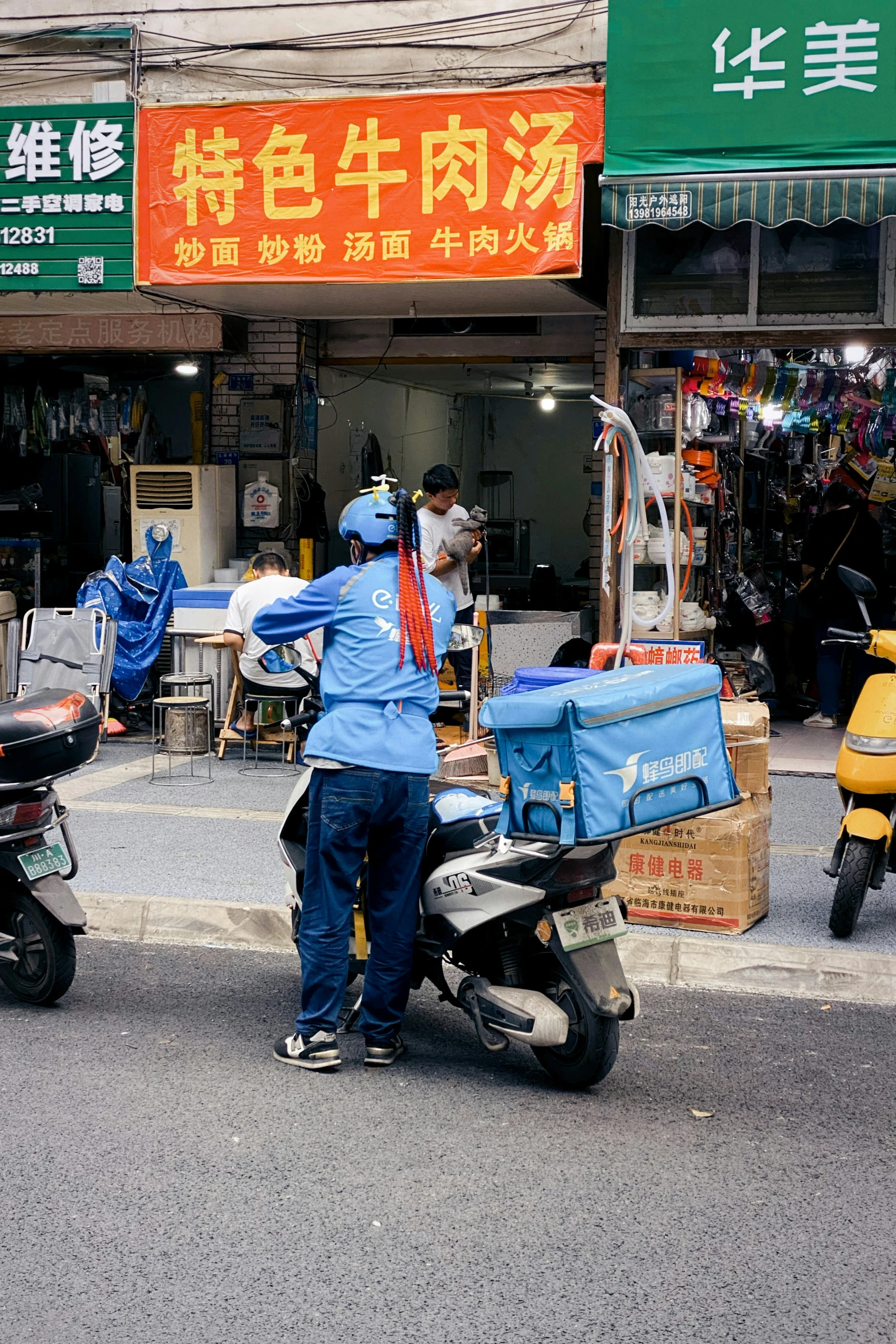 an asian man hing another scooter past a street vendor