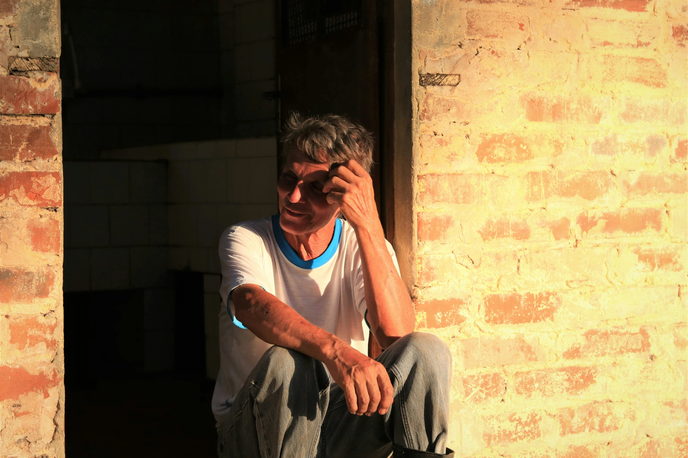 an older man sitting by a doorway, with his foot propped against his chin