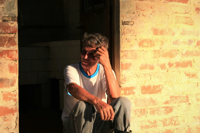 an older man sitting by a doorway, with his foot propped against his chin