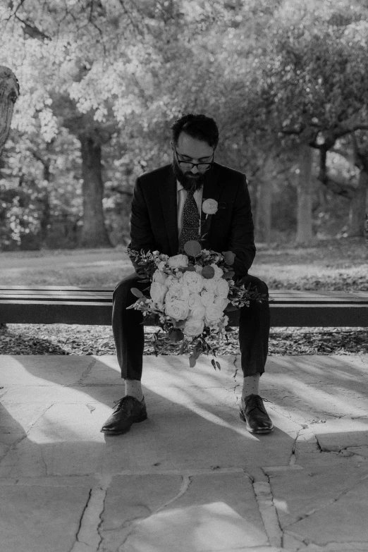 black and white image of man in suit sitting on a park bench