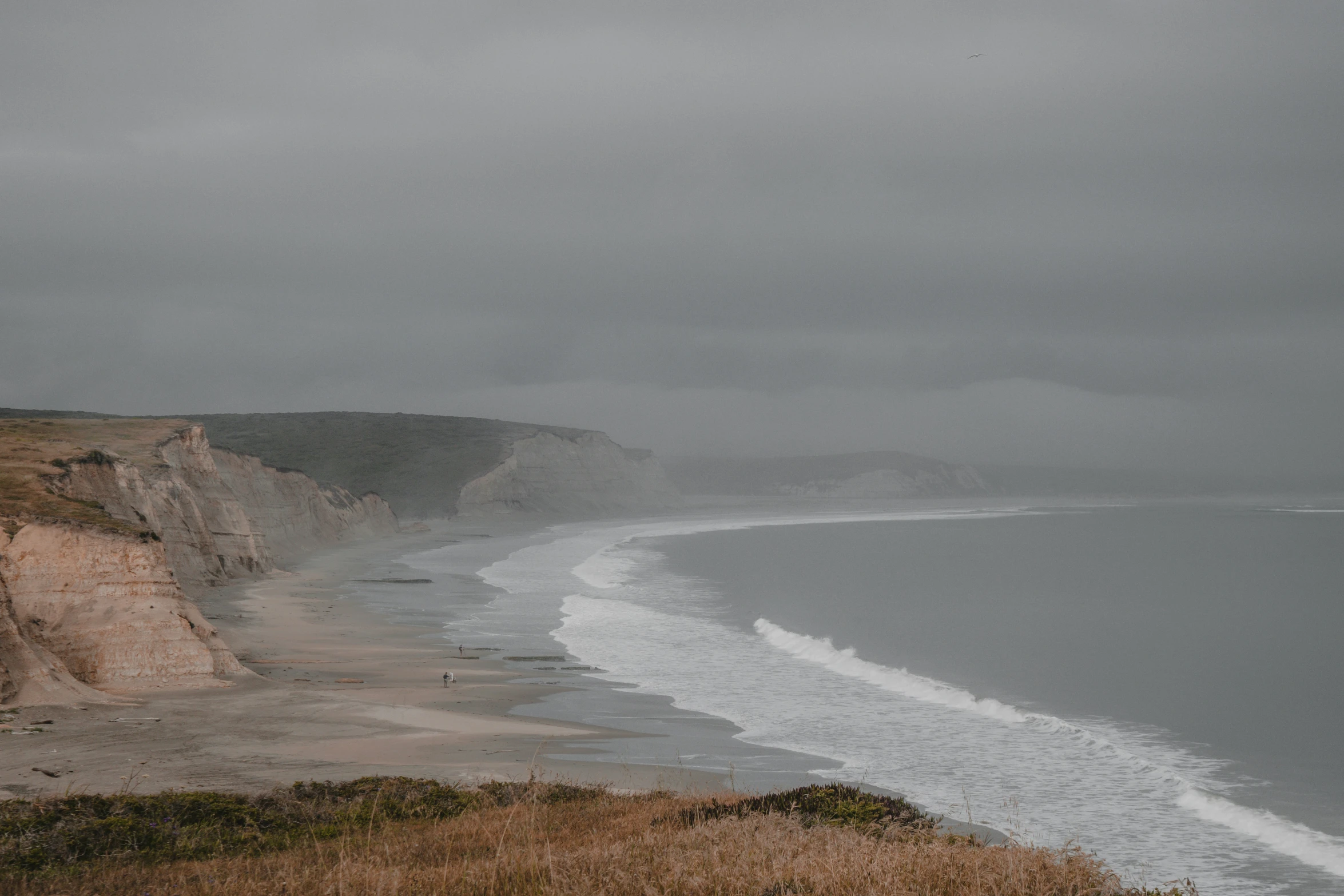 a body of water near a cliff on a cloudy day