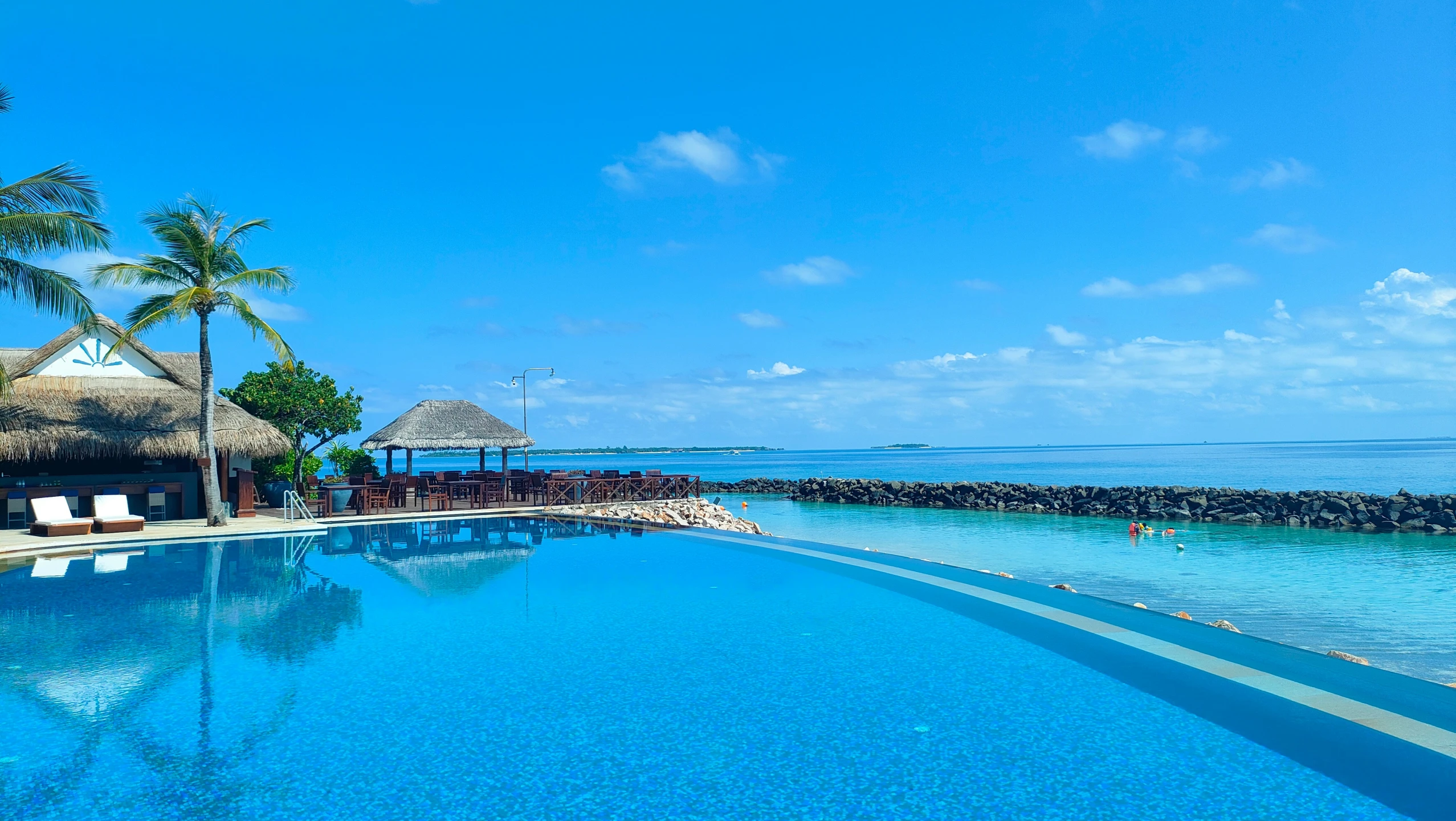 a long pool that has lounge chairs near the ocean