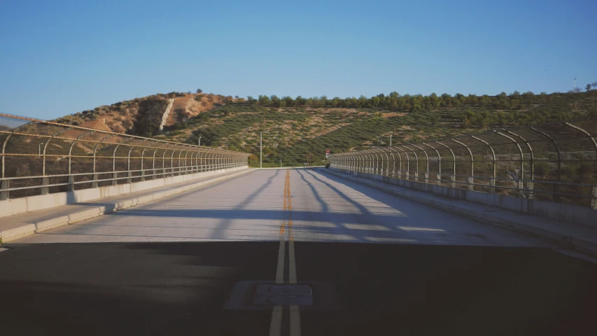 an empty street next to a hillside with trees