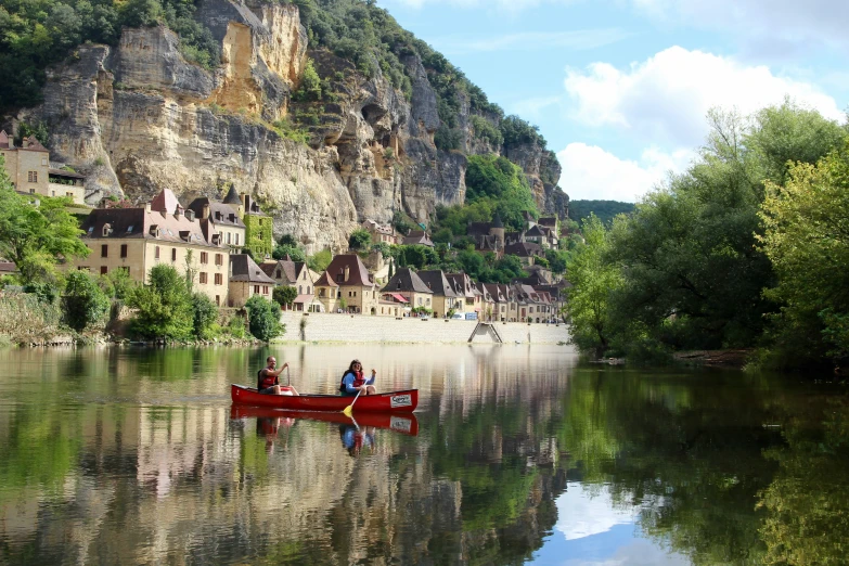 a couple in a red canoe going down a river by some small village