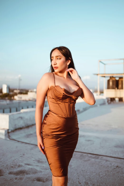 a woman in brown dress standing on cement and looking off into the distance