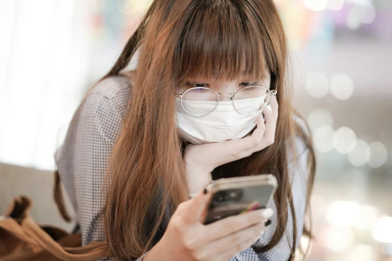 a woman looking at her cell phone wearing a protective mask