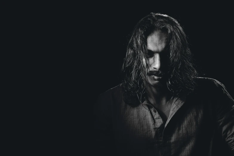 a man with long hair standing in a dark room