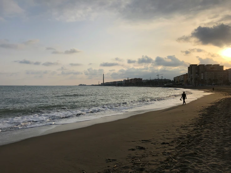 man walking in the sand of a beach with waves coming in