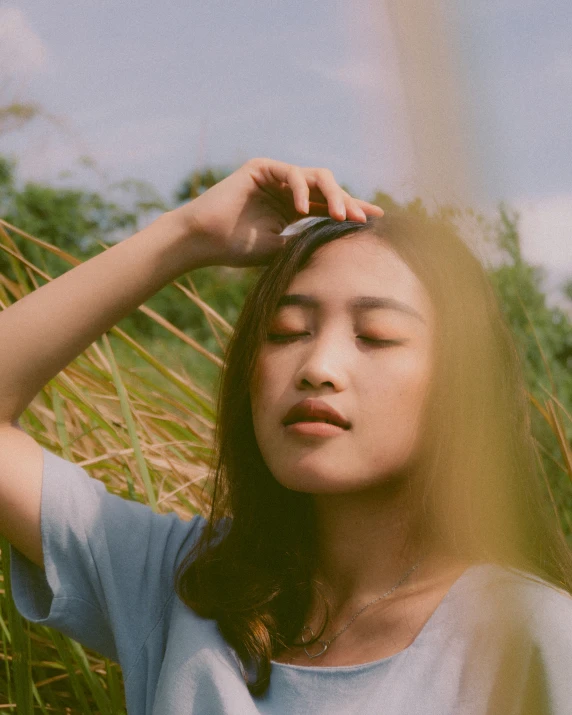 woman with eyes closed standing in grass with arms behind head