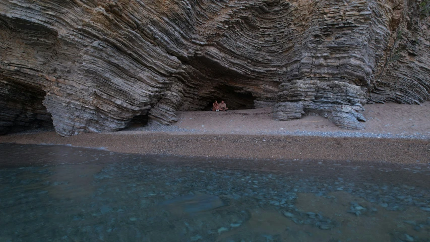 a cliff face, with two people standing on the edge of the cave