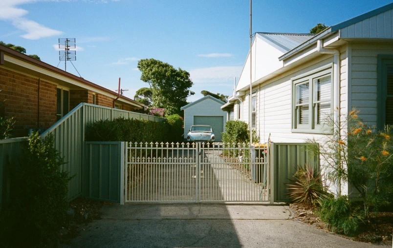 a fenced driveway is next to the house and another yard is seen behind it