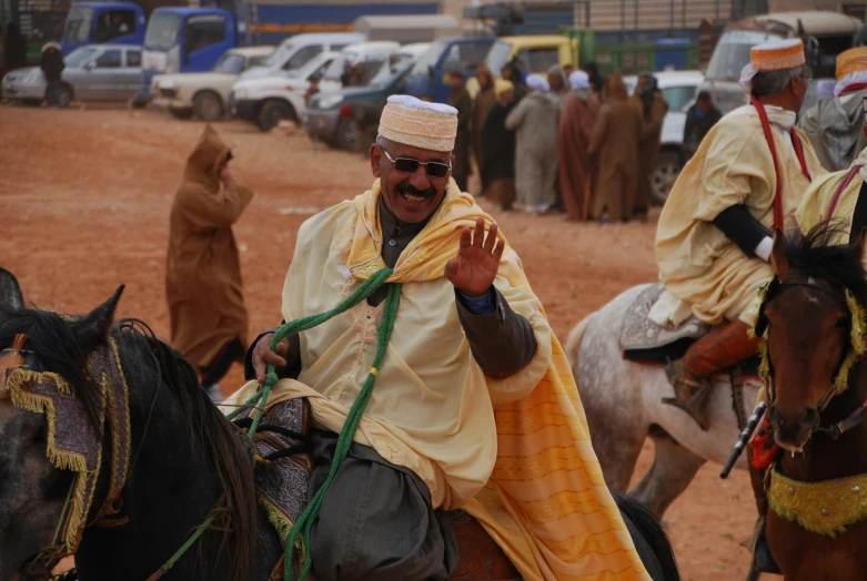 man dressed in traditional arab attire sitting on a horse with other men nearby