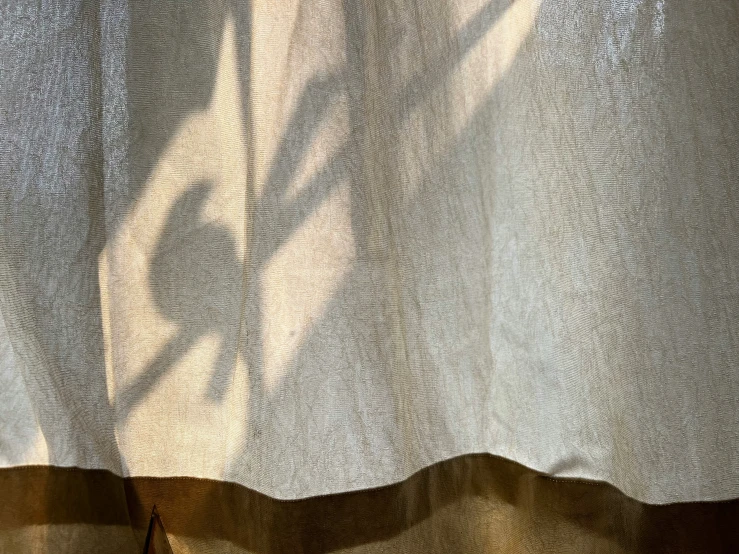 a window in the sunlight casts shadow over an open curtain