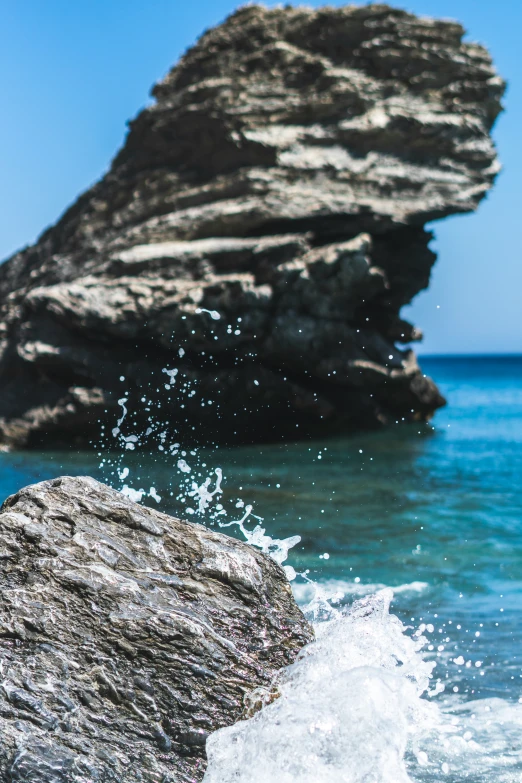 a bird flying over the water by a rock