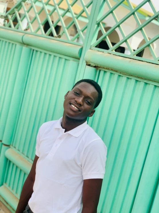 a smiling man is standing by a blue fence