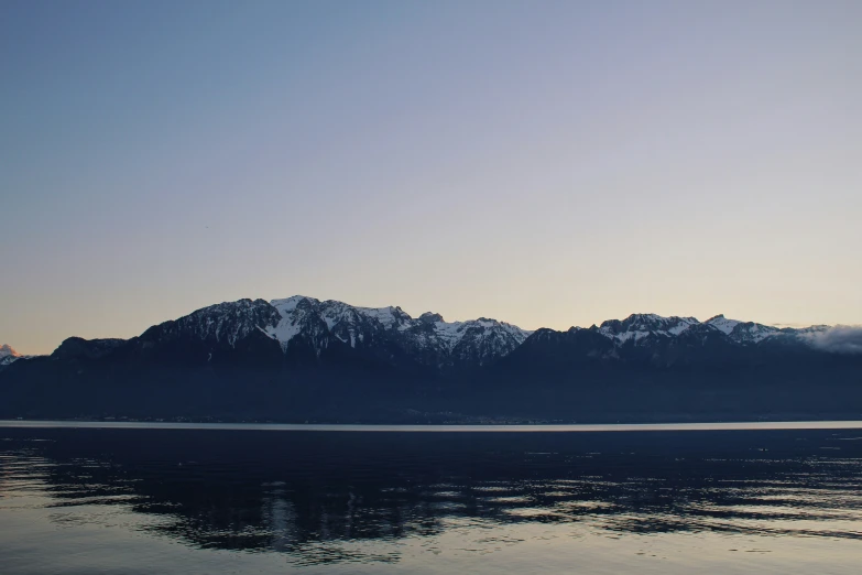 a mountain range is seen from the water at twilight