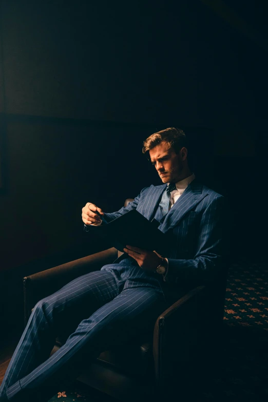 a man wearing a suit sitting in the dark, writing on a paper