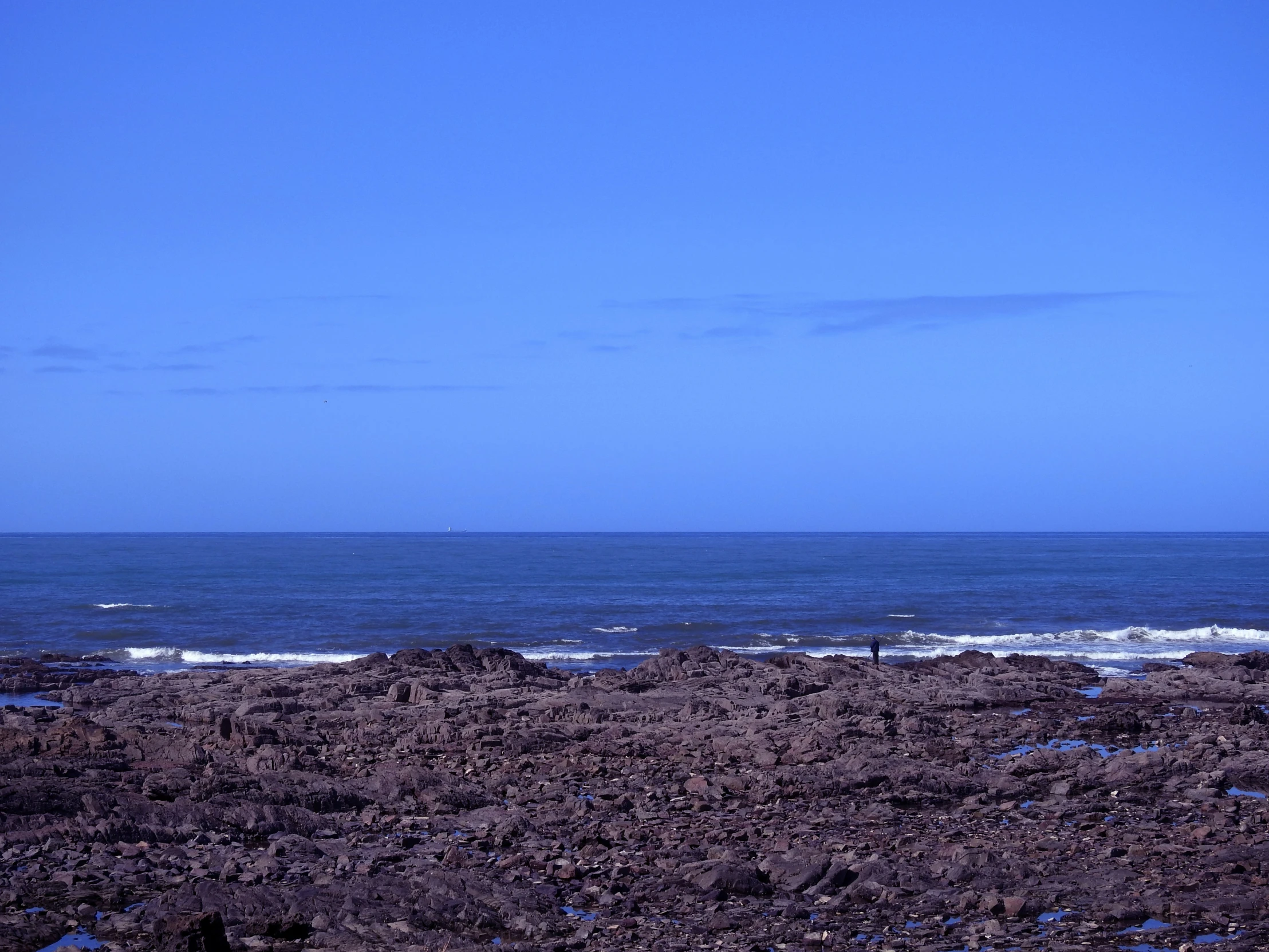 two people on the beach in the distance with a surf board