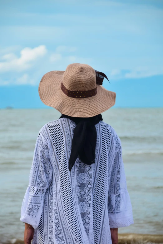 the woman in hat is walking along the beach