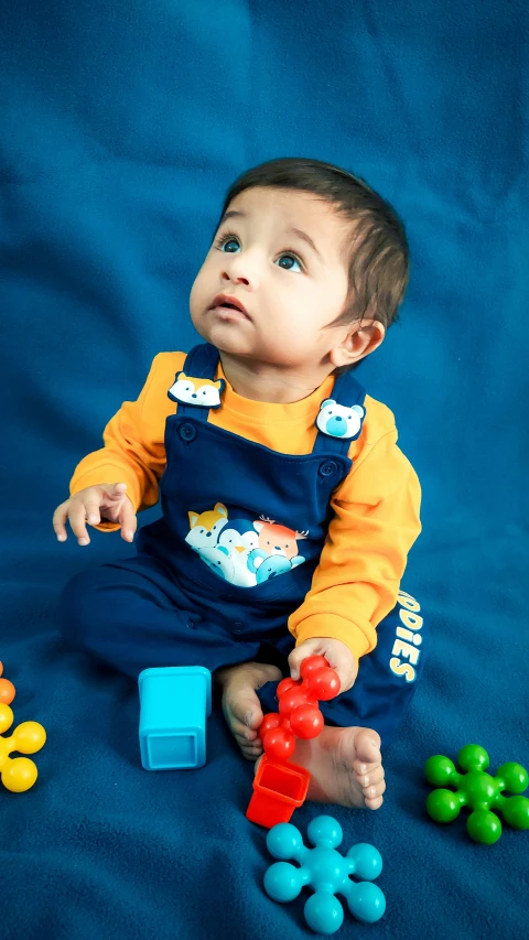 a baby in overalls playing with toys on a blue blanket