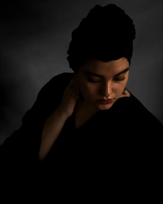 a woman with her hand on her right ear and a dark background
