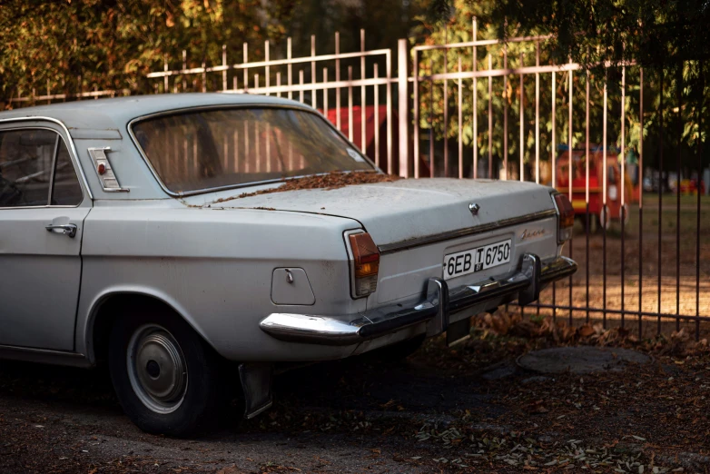 an old white car sitting next to a fence