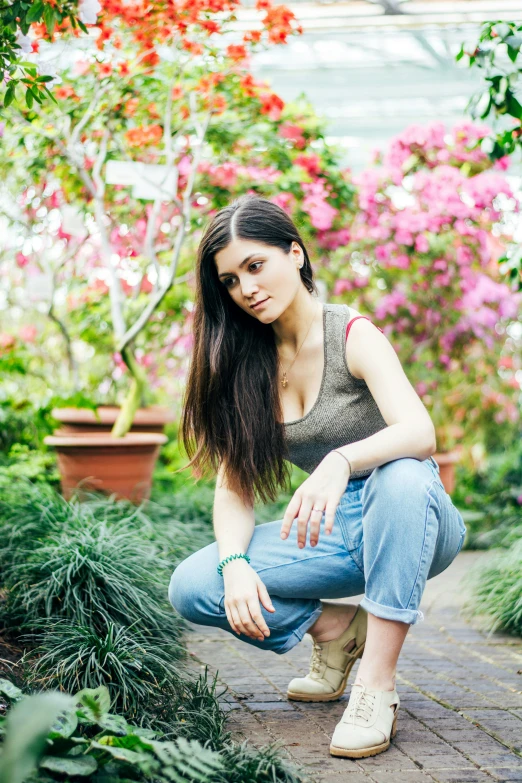 a beautiful young lady crouches down near many flowers