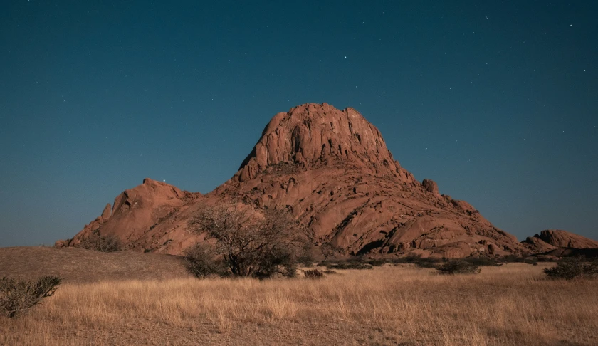 a big rock in the desert surrounded by dry grass