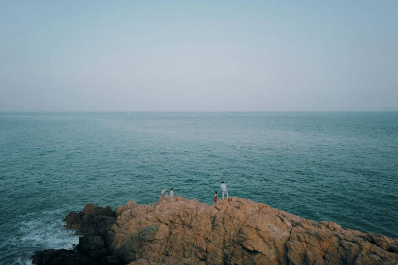 two people standing on a rocky cliff in the ocean