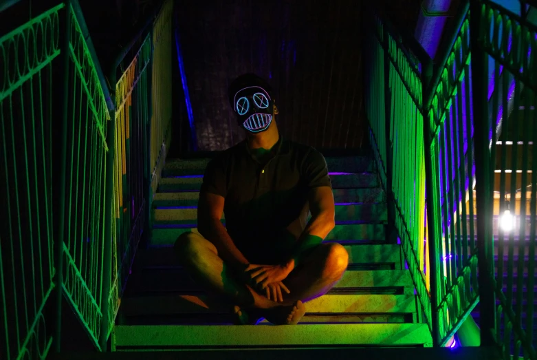 a man sitting on top of stairs in front of neon lights