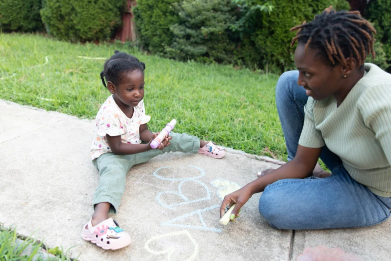 a woman holding a baby who is sitting on the ground and drawing