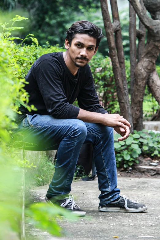 man in black shirt and jeans leaning on bench in front of trees