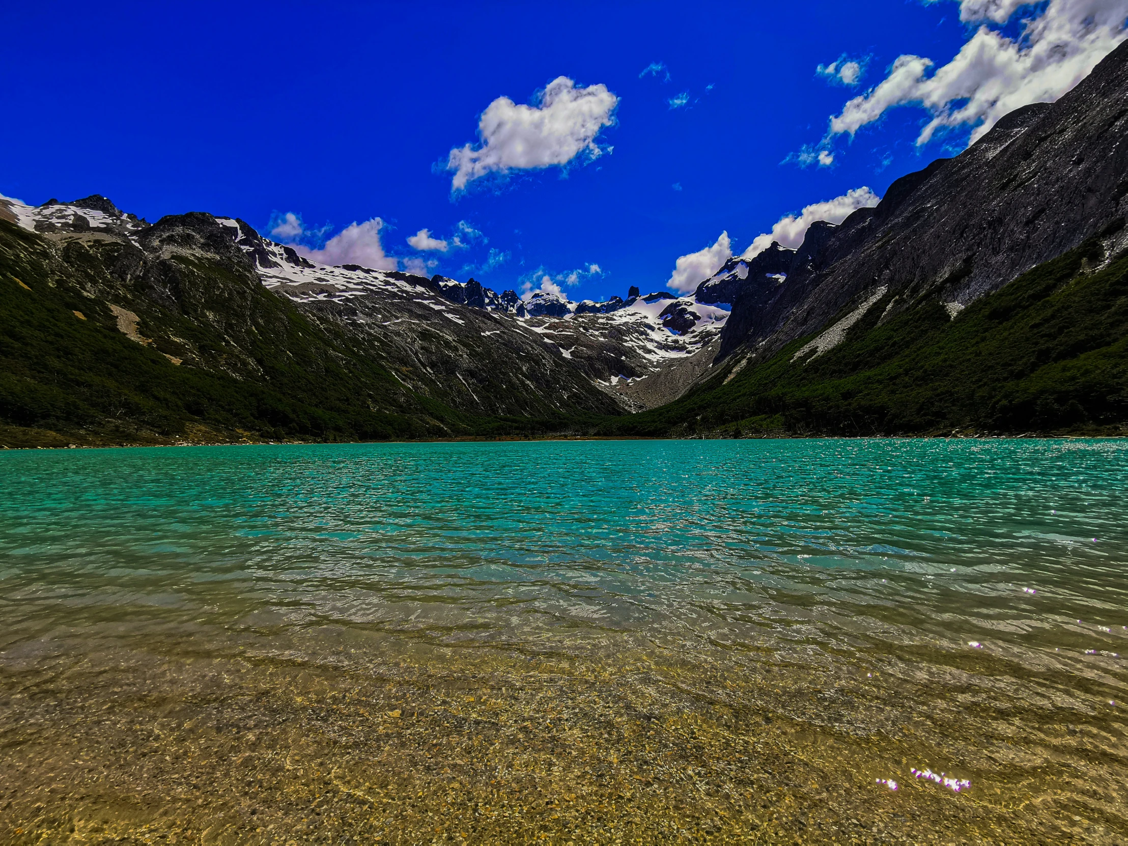 blue water in a mountains range with green algae on bottom